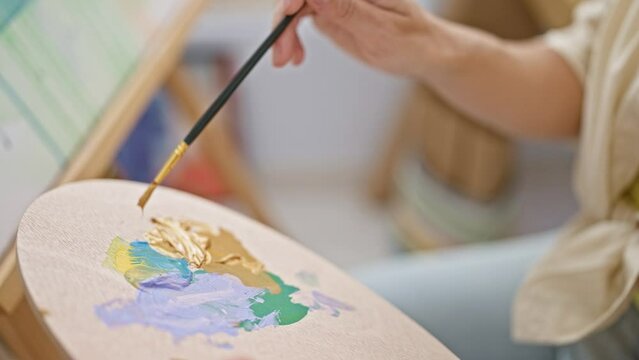 Young blonde woman artist mixing color on palette at art studio