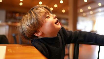 One small boy sitting at restaurant waiting for food to arrive feeling impatient and idle but with...