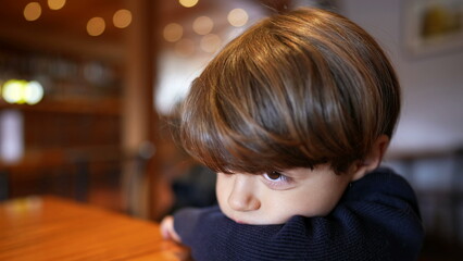 Pensive little boy leaning on table with deep introspective emotion. Close-up face of a thoughtful...