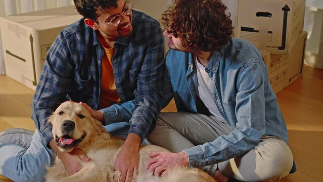 A young multi-ethnic couple of gay boys cuddle and play with their dog, a golden retriever.
Concept of home, love for animals and family