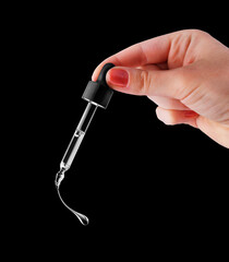 Female hand holds a cosmetic pipette with dripping drop close up on a black background