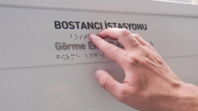 Hand of blind person touch and read Braille alphabet on text plate with his hands at the entrance of train platform in Istanbul, Turkey. Close up of mans fingers touching the relief of points