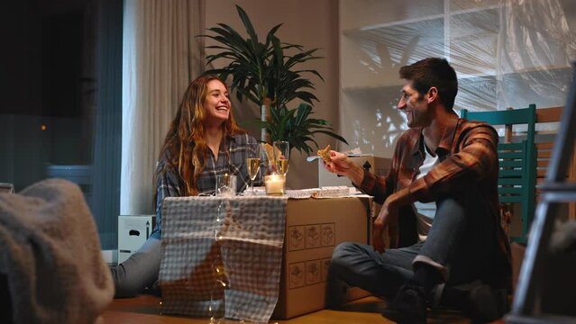 A Beautiful Couple Has Their First Dinner In Their New Home, Eating Pizza And Toasting With Wine