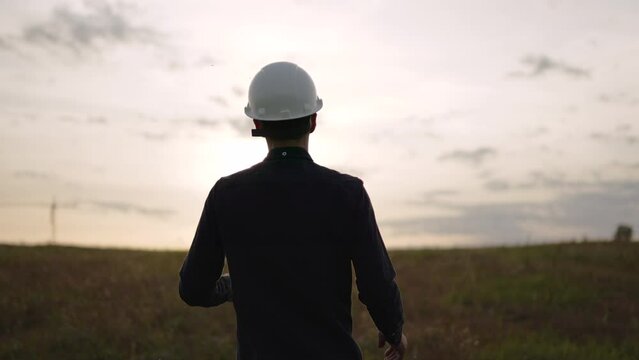 Unrecognizable builder takes off helmet as he walks towards sunset, rear view. Last working day and subsequent dismissal. Concept of violation of workers rights, refusal to perform work duties.