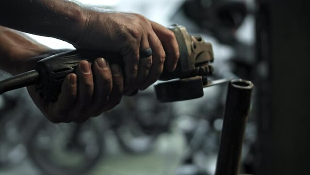 hands hold grinder in dark workshop and cut steel pipes with yellow sparks