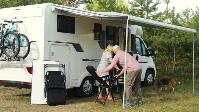 A man and a woman spread out outside a motorhome at a summer campsite