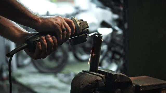 hands hold grinder in dark workshop and cut steel pipes with yellow sparks