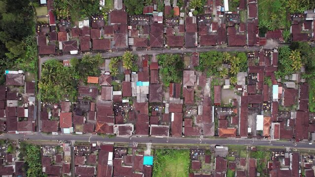 Typical Balinese village, top-down aerial panning shot, two parallel streets and many one-storey buildings. Traditional house compounds with most of building roofs covered with tiles.