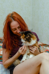 Red-haired girl with her lovely calico cat. Owner holds pet in hands.