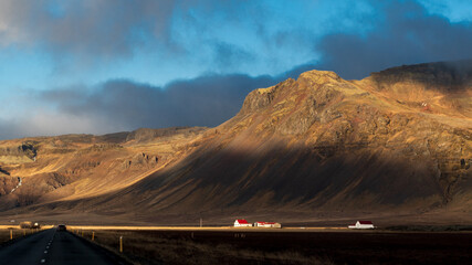 Paysage islandais ensoleillé et contrasté avec des maisons blanches aux toits rouges