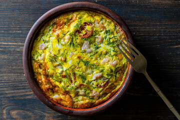 Ceramic bowl with vegetable frittata, simple food. Frittata with egg, tomato, pepper, onion, shrimps and cheese on wooden table, closeup, top view. Italian egg omelette