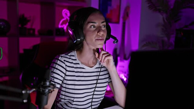 Excited young hispanic woman, a gaming numero uno! beautifully engrossed playing video game, wearing headset, fingering her pointy idea with a happy face in the dark home gaming room.
