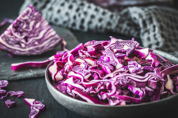 Obraz na płótnie Canvas Fresh red cabbage, cut into pieces and strips, on gray table