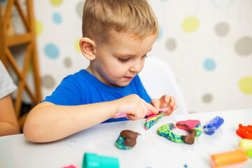 Little boy enthusiastically plays with plasticine, play dough on white table