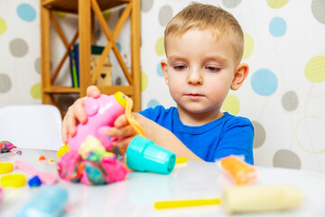 Little boy enthusiastically plays with plasticine, play dough on white table