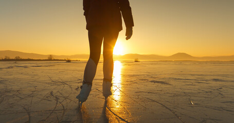 LENS FLARE, SILHOUETTE: A cold winter day with a woman skating in golden light - obrazy, fototapety, plakaty