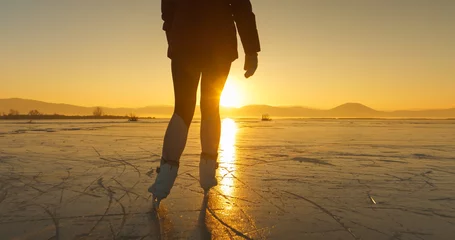 Gordijnen LENS FLARE, SILHOUETTE: A cold winter day with a woman skating in golden light © helivideo