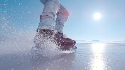 LENS FLARE, CLOSE UP: Flying pieces of crushed ice when guy brakes on skates