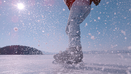 LENS FLARE, CLOSE UP Male ice skater sprays pieces of crushed ice when he brakes