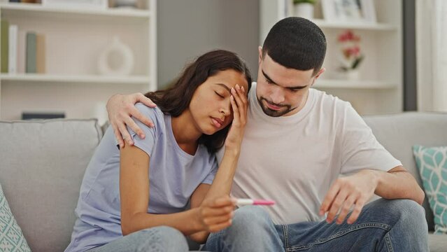 Beautiful couple hugging, upset at home, holding positive pregnancy test, an unexpected family problem in their comfortable living room