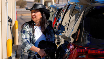 A fierce cowgirl at a gas station, her hat and clothing exuding western charm, she fills up with...