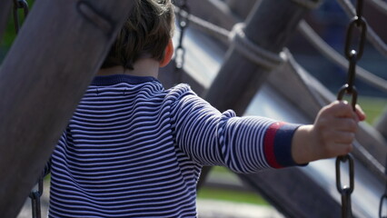 Child takes hold of chain at playground structure, losing equilibrium, learning to play. Small boy...