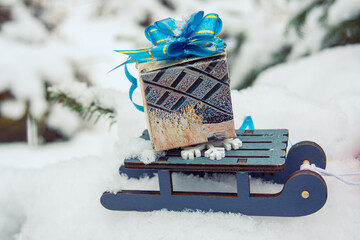 winter holiday background with a toy sled carrying a gift against the backdrop of snowy weather and snow