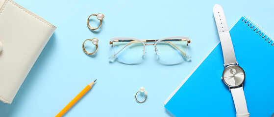 Eyeglasses with jewelry rings, wristwatch and stationery on light blue background