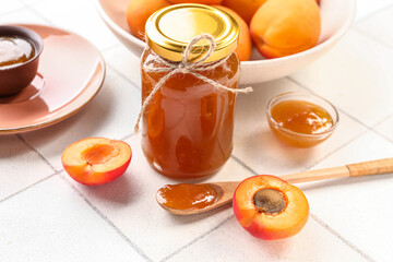 Jar and bowl with sweet apricot jam on white tile background