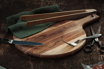Holzbrett mit Gabel, Messer, Stofftuch und Schere auf Holztisch