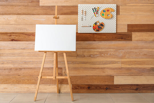 Easel and pegboard with drawing tools on wooden wall in studio