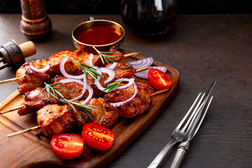 Pork kebab with barbecue sauce and tomatoes and a glass of red wine on a dark table