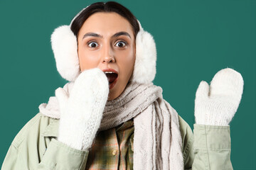 Surprised young woman in winter clothes on green background, closeup