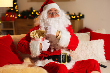 Merry Christmas. Emotional Santa Claus with popcorn bucket watching TV on sofa at home
