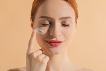 Beautiful young woman with sun protection cream on her face against beige background, closeup