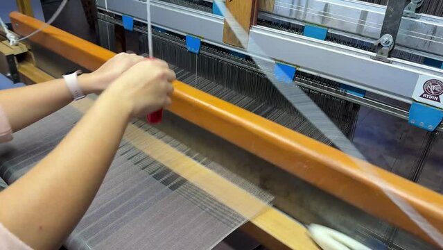 Industrial textile factory. Close up of thick white threads moving through the loom , woman making production on a traditional loom