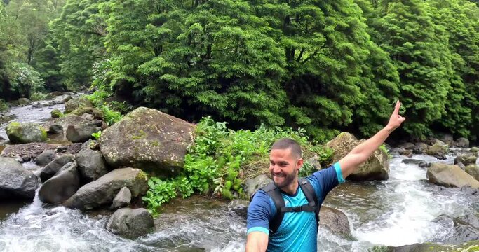 A man in the middle of a river surrounded by a thick forest in the island of Sao Miguel in Azores, Portugal, in the path to arrive to the 'Cascata do Salto do Prego'