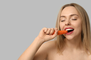 Young woman eating carrot on light background, closeup