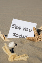 SEA YOU SOON text on paper greeting card on background of starfish seashell summer vacation decor. Sandy beach sun coast. Holiday concept postcard. Getting away Travel