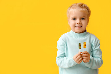 Cute little girl with sweet lollipops on yellow background