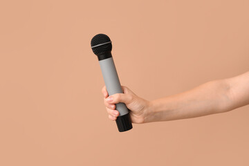 Female hand with microphone on beige background, closeup