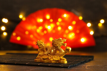 Golden dragon figurine on bamboo mat with red paper fan and blurred lights in background