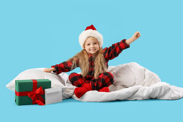 Cute little girl in Santa hat stretching on blue background