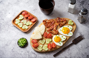 Fototapeta na wymiar Fresh breakfast with fried eggs, fried bacon slices, bread slices and vegetables in the form of heart for Valentine's day holiday