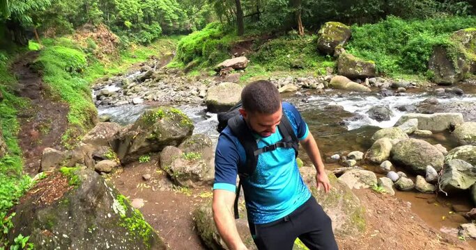 A man running in a path in the middle of a thick forest close to a river in the island of Sao Miguel in Azores, Portugal, in the path to arrive to the 'Cascata do Salto do Prego'