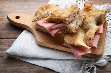 Wholemeal focaccia with mortadella on wooden background with cutting board and napkin, close-up. - 683060284
