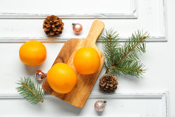 Wooden board with tasty oranges and fir branches on white background