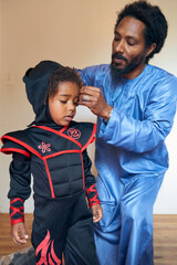 Obraz premium Portrait of Black Father helping Child put on Costume 