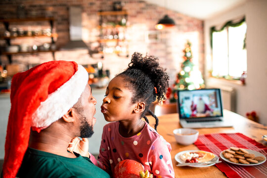 Father and Daughter Sharing a Festive Kiss with Holiday Decorations and Video Call in Background