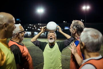 Senior man balancing soccer ball on head with friends on field